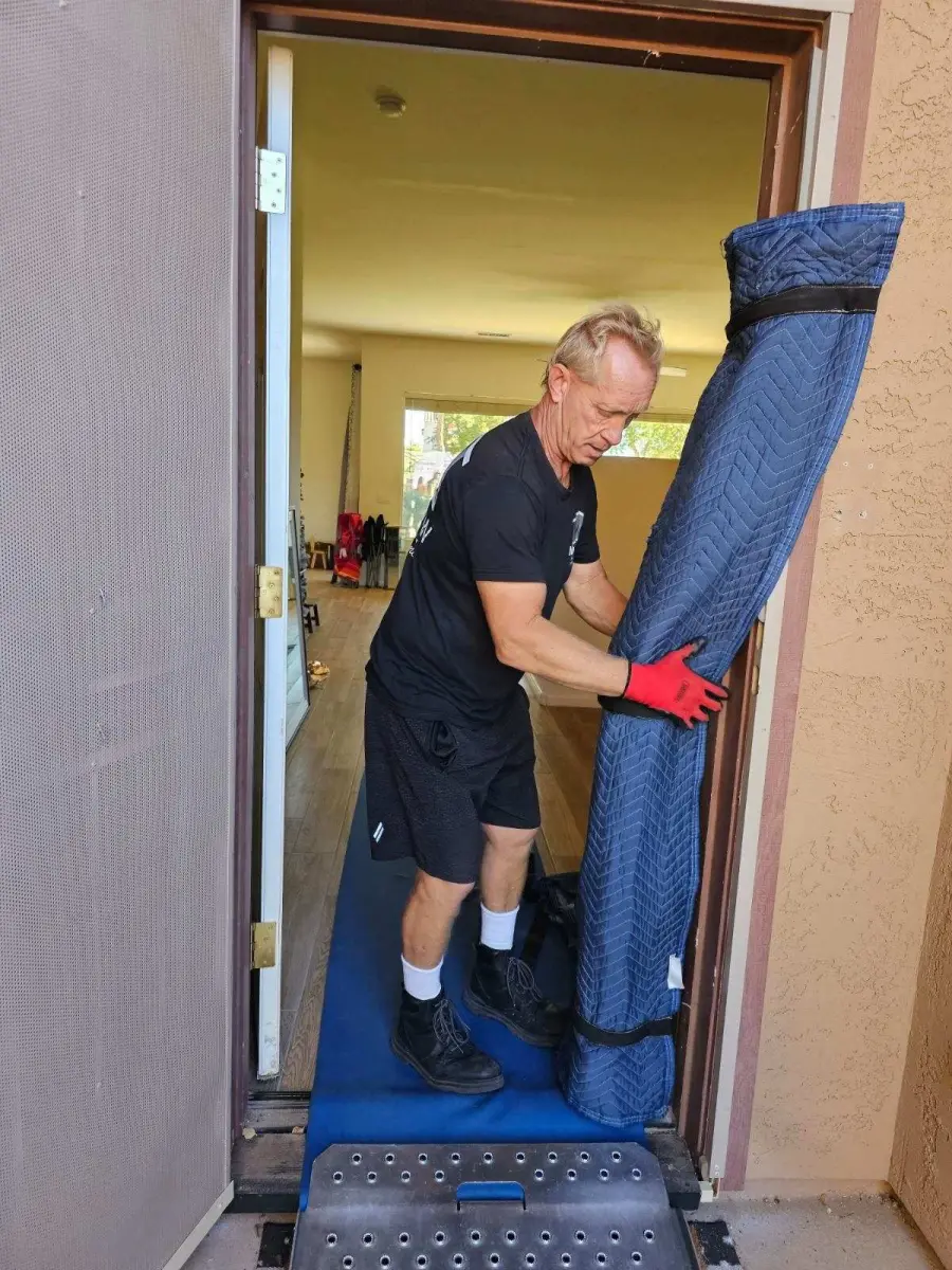 A mover guides a padded piece through a front door on a dolly