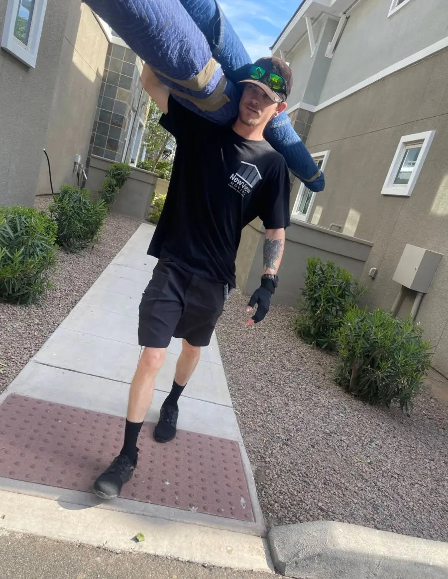 A NewView mover carries a padded item on his shoulder down a garden path