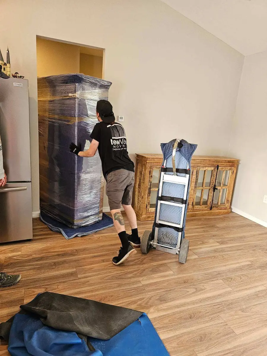 A refrigerator wrapped in pads and plastic on a hand truck in a kitchen