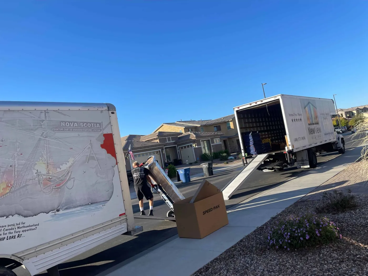 A NewView mover loads furniture from a rental truck outside a home flying an American flag