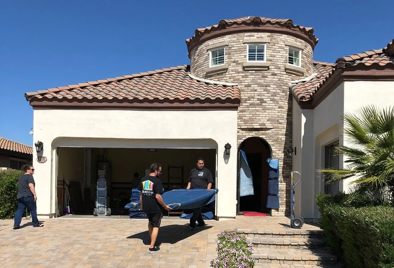Three NewView movers carry a moving pad into a two-story Arizona home with a tiled roof